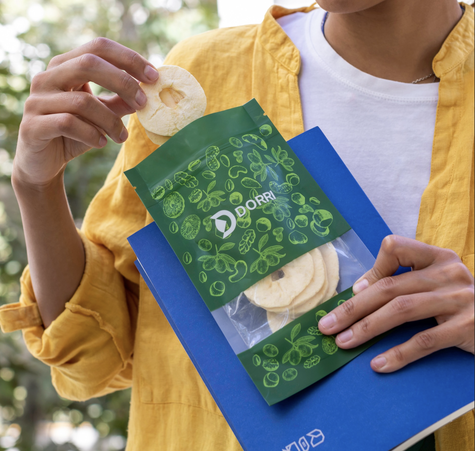 Lifestyle — a person in a yellow shirt holding a green Dorri pouch of dried apple rings, taking one out
